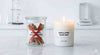 Słoik z laskami cynamonu oznaczony jako „restricted fragrance” stoi obok zapalonej świecy z wosku oliwkowego z etykietą „safe & pure olive wax”, podkreślając kontrast między potencjalnie drażniącymi dodatkami a bezpieczniejszym składem świecy.