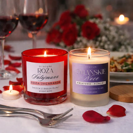 Dwie palące się świece Oyasumi Róża Sulejmana i Omańskie Noce na zastawionym stole z winem i płatkami róż, wosk oliwny polski producent.