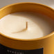 Zbliżenie na bawełniany knot i idealnie gładką taflę nienaruszonej świecy Egipski Sen w matowej, żółtej oprawie.