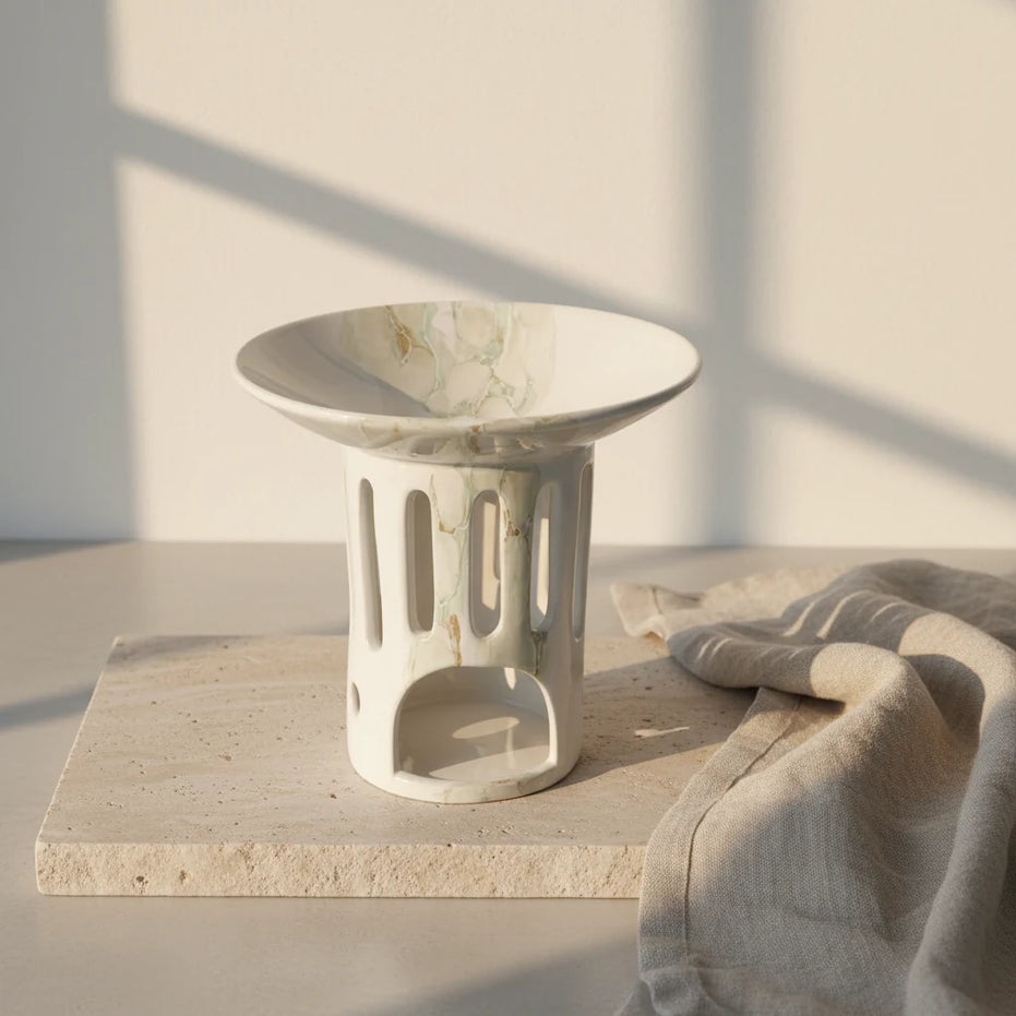 Nowoczesny biały marmurkowy ceramiczny kominek do wosków zapachowych OYASUMI na kamiennej podstawie w ciepłym świetle.