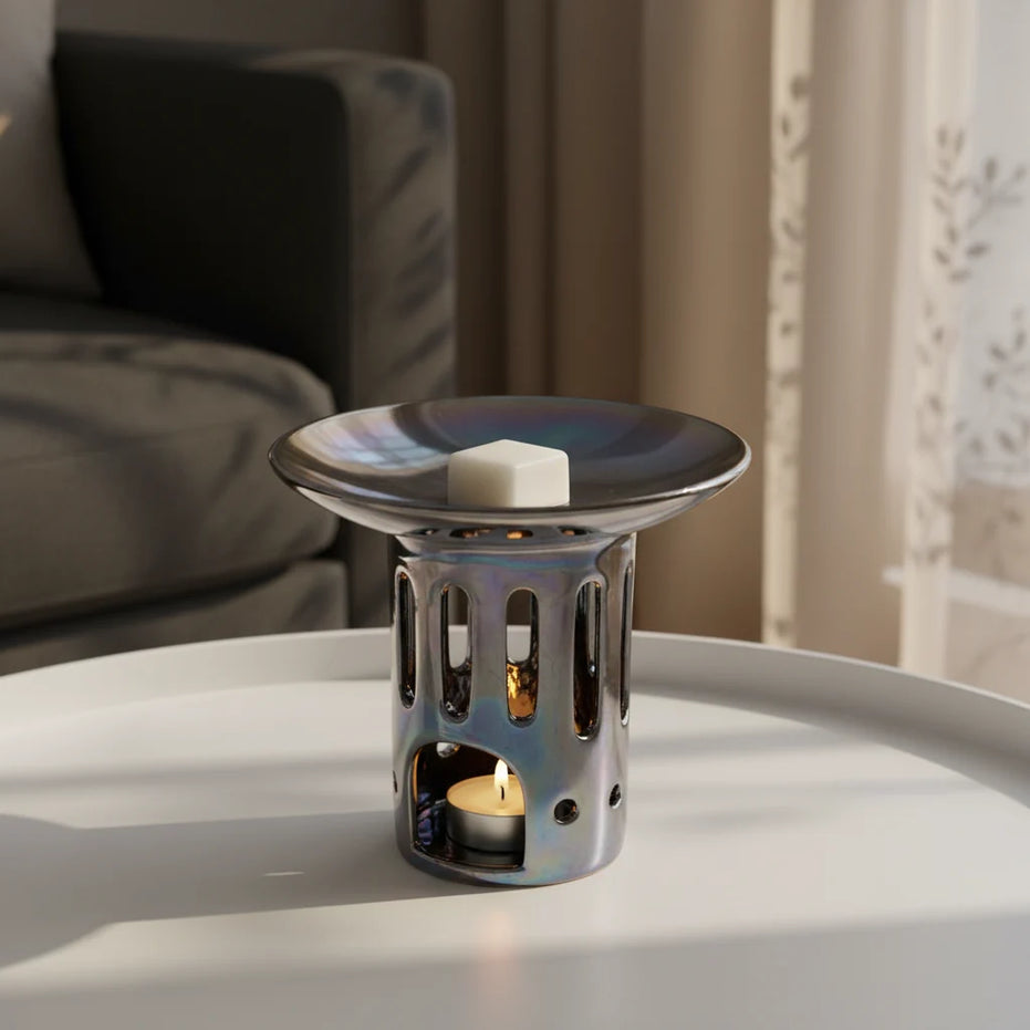 Grafitowy ceramiczny kominek zapachowy OYASUMI z kostką wosku oliwkowego i świeczką tealight ustawiony na białym stoliku.