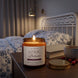 Płonąca świeca zapachowa Dzikie Polesie oyasumi w szklanym słoiku na nocnej szafce wieczorem, obok książka i żurawiny – zapach żurawinowy