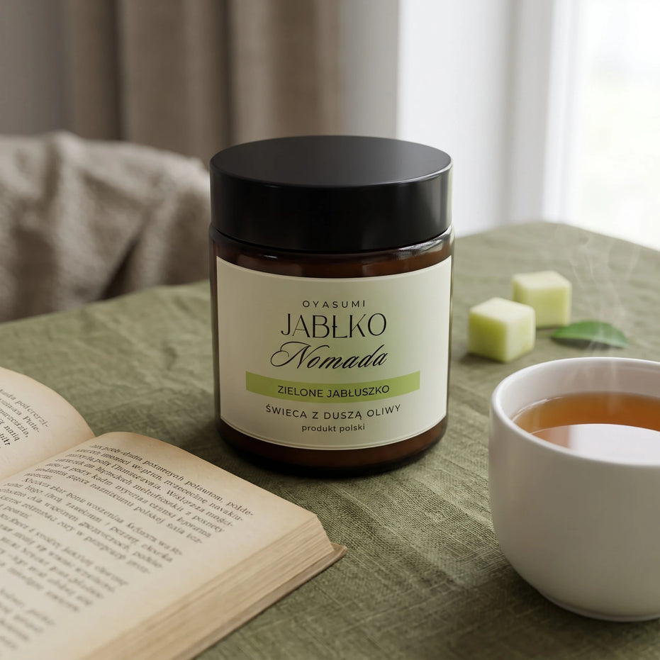 Świeca zapachowa OYASUMI Jabłko Nomada 90 ml z książką, kostkami jabłka i filiżanką kawy.