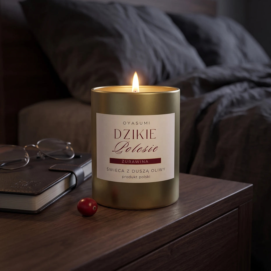 Płonąca złota świeca Dzikie Polesie wyeksponowana na drewnianym stoliku nocnym obok eleganckiej książki i okularów. Świeca o aromacie żurawiny zabiera w niezapomnianą podróż zmysłów, a wykorzystany wosk oliwny o europejskim pochodzeniu zapewnia bezpieczny i głęboki relaks.