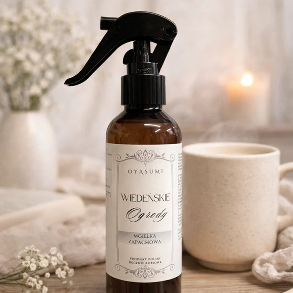 Mgiełka zapachowa Wiedeńskie Ogrody 200 ml OYASUMI w przytulnej aranżacji z kubkiem ciepłego napoju i palącą się świecą.
