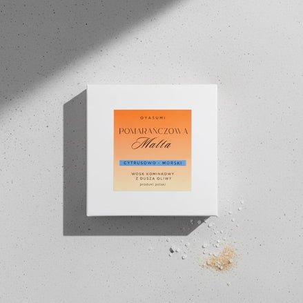 Białe pudełko wosku zapachowego Oyasumi Pomarańczowa Malta na szarym tle obok kryształków soli morskiej.