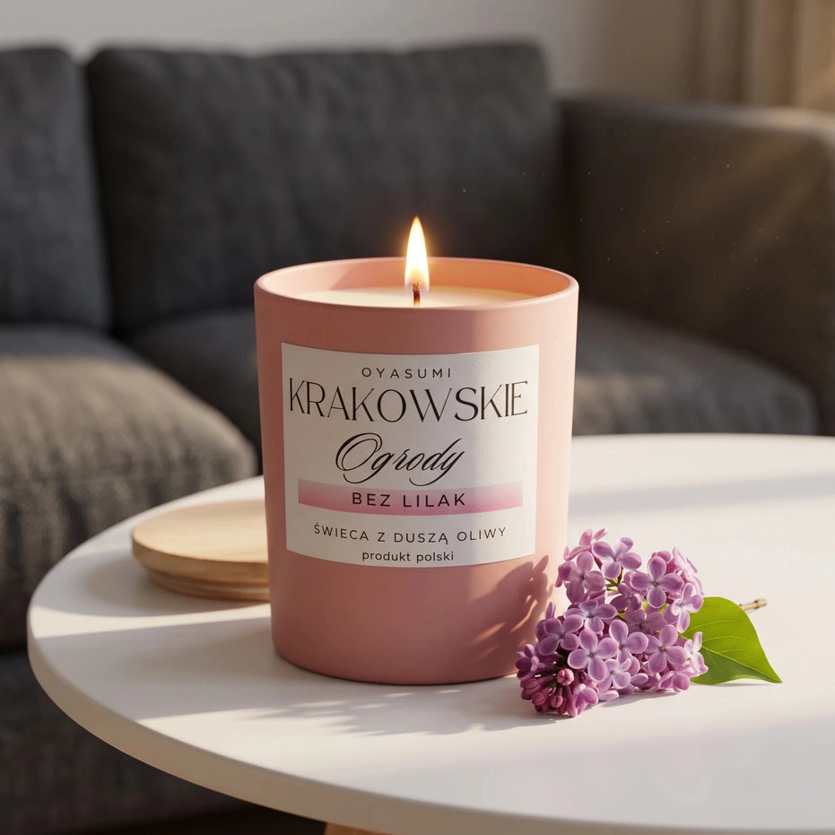 Świeca zapachowa z wosku oliwkowego Bez Lilak Oyasumi Krakowskie Ogrody w różowym ceramicznym słoiku z drewnianą pokrywką i kwiatem bzu na stoliku